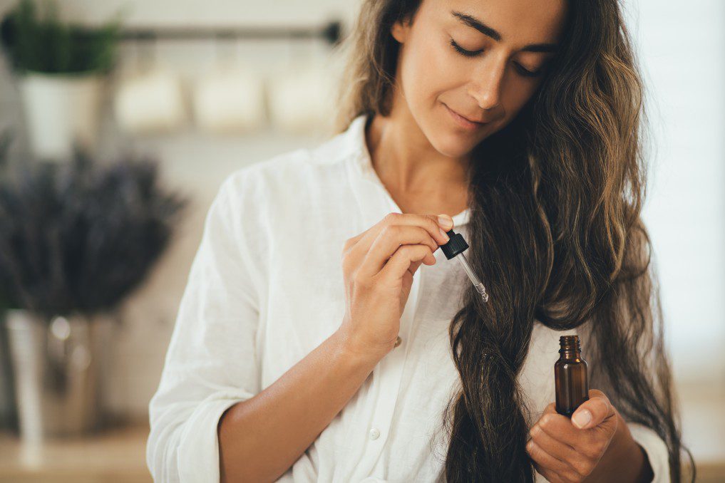 Óleos essenciais para crescimento dos cabelos, mulher passando oleo essencial no cabelo